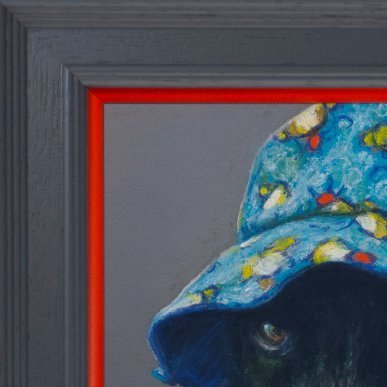 Close up picture of a cocker spaniel wearing a colourful bucket hat on a grey background in a grey frame with orange border