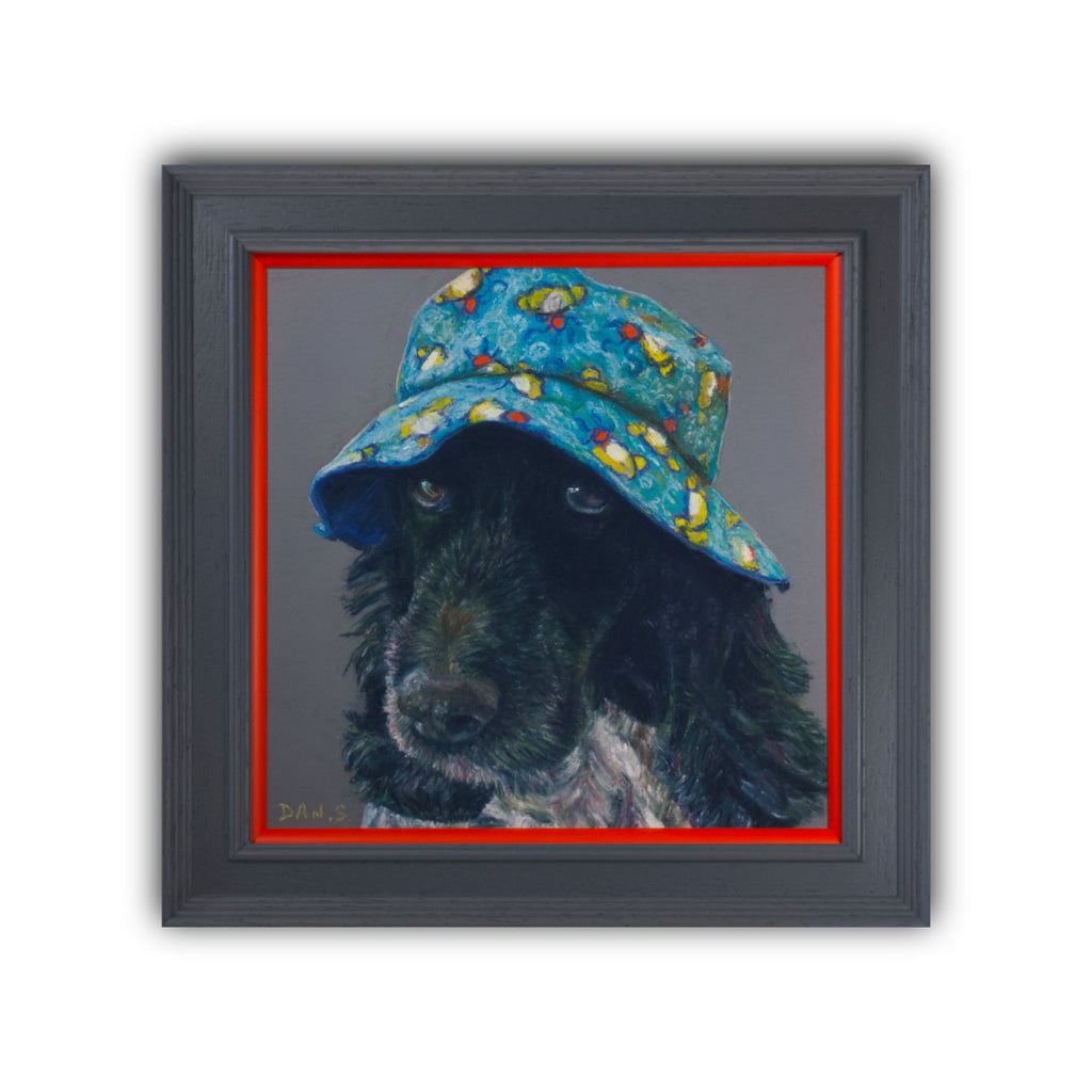 Picture of a cocker spaniel wearing a colourful bucket hat on a grey background in a grey frame with orange border